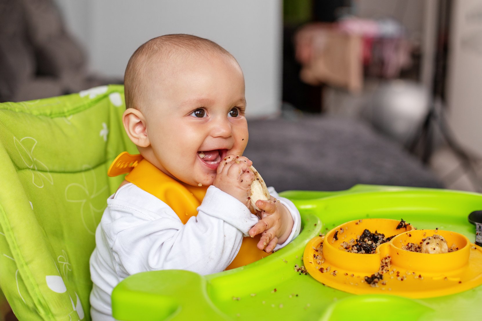 Baby sitting in high chair, eating puree or porridge. Baby eats complementary foods